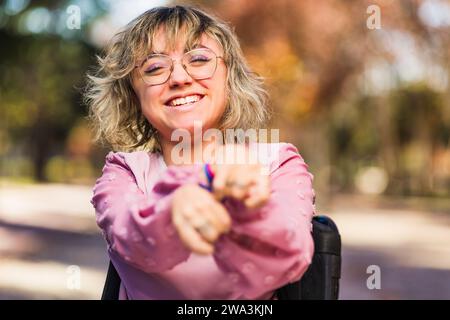 Junge Frau mit Zerebralparesebehinderung auf Rollstuhlgrüße und Lächeln. Soziale Eingliederung Stockfoto