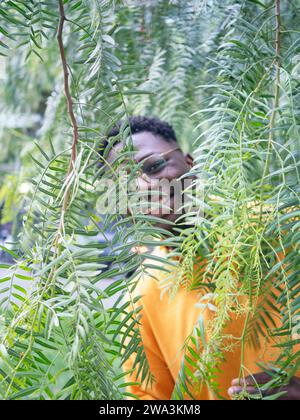 Porträt eines jungen Afroamerikaners, der hinter der Vegetation lächelt. Künstlerisches Porträt Stockfoto