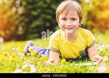 Glücklicher kleiner Junge, der an einem sehr sonnigen Tag im Park im Freien einen Tablet-PC spielt Stockfoto