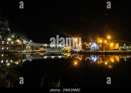 Papierfabrik in der Nacht. Winterfoto einer kleinen Fabrik mit Reflexion in einem See. Nachtszene in Bengtsfors, Schweden, Europa Stockfoto