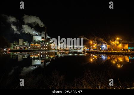 Papierfabrik in der Nacht. Winterfoto einer kleinen Fabrik mit Reflexion in einem See. Nachtszene in Bengtsfors, Schweden, Europa Stockfoto