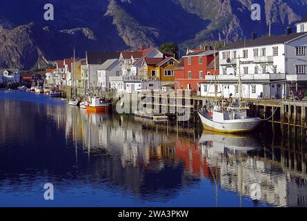 Fischerboote und Holzhäuser spiegeln sich im kleinen Hafen von Henningsvaer, Angeln, Abendlicht, Lofoten, Nordland, Norwegen, Europa Stockfoto