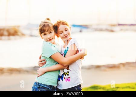 Zwei 9-10-jährige Mädchen spielen draußen zusammen, umarmen sich gegenseitig, Golden Hour Stockfoto