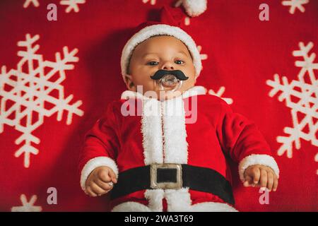 Weihnachtsporträt eines entzückenden Neugeborenen, das das Weihnachtsmannskostüm trägt, auf einer Schneeflockendecke liegend, Blick von oben. Stockfoto