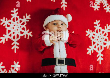 Weihnachtsporträt eines entzückenden Neugeborenen, das das Weihnachtsmannskostüm trägt, auf einer Schneeflockendecke liegend, Blick von oben. Stockfoto