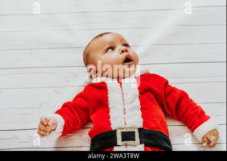 Porträt eines süßen Jungen, der auf weißem Hintergrund liegt, das Weihnachtsmann-Outfit trägt und aufblickt Stockfoto