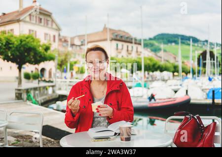 50-60-jährige Frau, die sich im Freien ausruht und im Café am Genfer See Buch liest Stockfoto