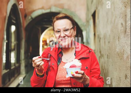 50-60-jährige Frau isst draußen Eis Stockfoto