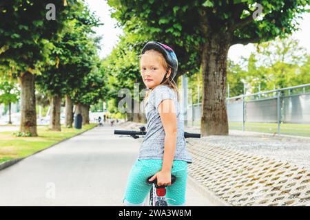 Kleines Mädchen, das im Park auf dem Fahrrad sitzt und über die Schulter blickt Stockfoto