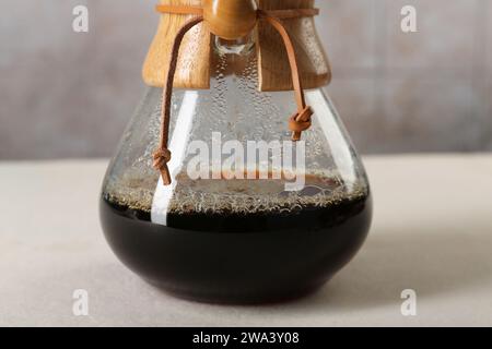 chemex-Glaskaffeemaschine mit leckerem Tropfkaffee auf weißem Tisch, Nahaufnahme Stockfoto