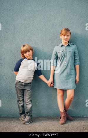 Außenporträt von 2 Modekindern, die vor blauem Hintergrund posieren, Porträt in voller Länge Stockfoto