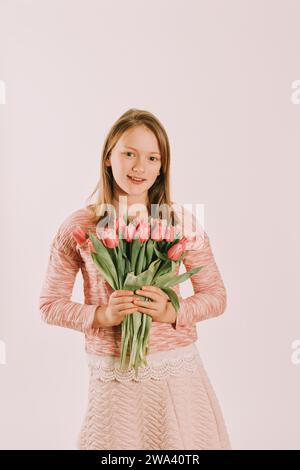 Studio-Bild eines süßen Jugendlichen Mädchens, das Sweatshirt trägt und rosa Tulpen hält Stockfoto