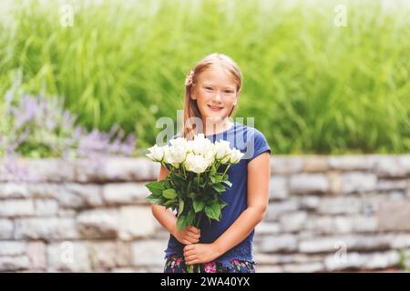 Außenporträt eines 9-jährigen Yong-Mädchens, das ein blaues T-Shirt trägt und einen frischen Blumenstrauß mit schönen weißen Rosen hält Stockfoto