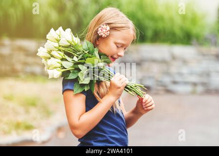 Außenporträt eines 9-jährigen Yong-Mädchens, das ein blaues T-Shirt trägt und einen frischen Blumenstrauß mit schönen weißen Rosen hält Stockfoto