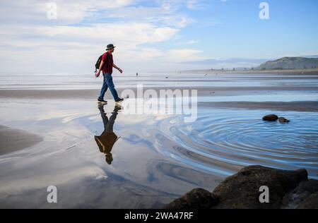 Mann, der im Sommer auf nassem Sand am Muriwai Beach läuft. Auckland. Stockfoto