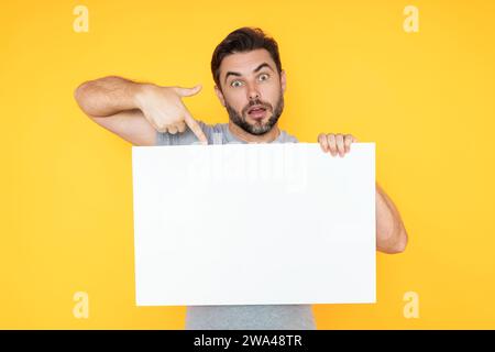 Ein Typ mit leerer Bannerwerbung, isoliert im Studiohintergrund. Ein Mann hält ein leeres Poster, auf dem ein Plakat mit dem Finger zeigt und mit dem Zeigefinger bewegt wird Stockfoto