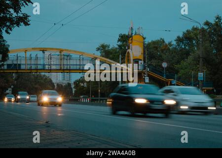 Verkehr auf der Autobahn in Bewegung. Verkehr in der Sommerabendstadt. Autos in Bewegung mit Lichtern entlang des Bürgersteigs. Urbane Szene mit Transport. Stadtstraße. Stockfoto