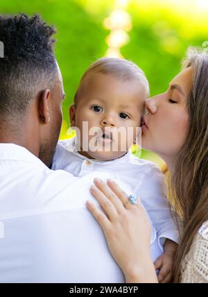 Mütter küssten das Baby. Nahporträt einer Mutter, die ein multirassisches Baby küsst. Mutter küsst Kind, Vater kümmert sich um Baby. Nahaufnahme des Gesichts von Mutter mit Biracial Stockfoto