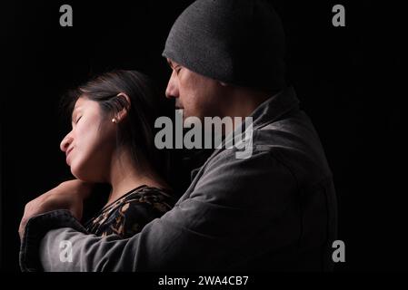 Mann umarmt die Frau von hinten auf einem dunklen Hintergrund und sie erwidert. Stockfoto