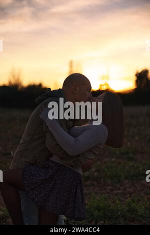 Ein Mann umarmt und küsst seine Freundin bei Sonnenuntergang in einer natürlichen Umgebung. Stockfoto