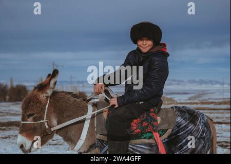 TAU SAMALY, KASACHSTAN - 23. DEZEMBER 2023: Kasachischer Junge reitet im Winter auf einem Feld in der Nähe von Tau Samaly in Kasachstan auf einem Esel Stockfoto