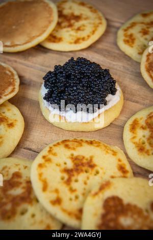 Blinis mit schwarzem Kaviar und Frischkäse, auf festlichem Gericht, Mini-Pfannkuchen, eine elegante Vorspeise Stockfoto