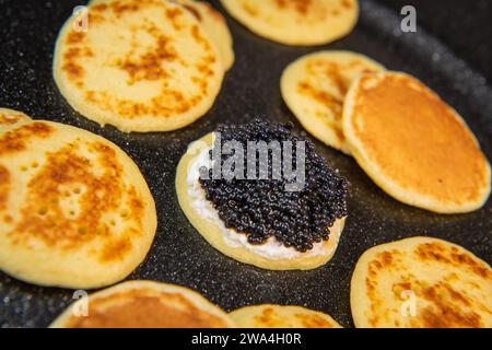 Blinis mit schwarzem Kaviar und Frischkäse, auf festlichem Gericht, Mini-Pfannkuchen, eine elegante Vorspeise Stockfoto