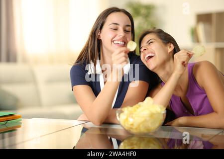 Zwei lustige Mitbewohner, die zu Hause lachen und Kartoffelchips essen Stockfoto