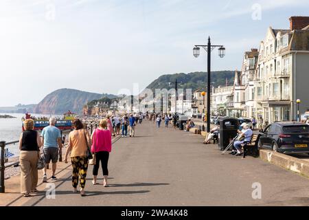 Sidmouth Dorset 2023, die Leute laufen entlang der Sidmouth Promenade am Meer mit jurastude im Hintergrund, England, Großbritannien Stockfoto