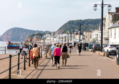 Sidmouth Dorset 2023, die Leute laufen entlang der Sidmouth Promenade am Meer mit jurastude im Hintergrund, England, Großbritannien Stockfoto