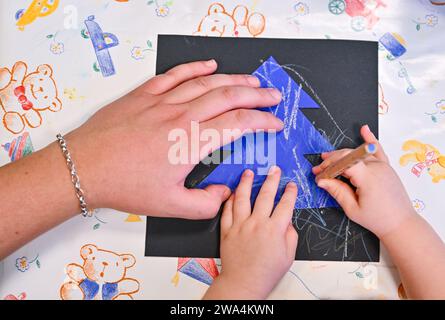 Spremberg, Deutschland. Dezember 2023. Ein Erzieher unterstützt ein Kindergemälde in einer Kindertagesstätte/einem Kindergarten. Quelle: Patrick Pleul/dpa/Alamy Live News Stockfoto