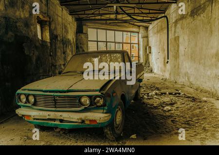 Verlassener Oldtimer, der in einer verfallenen Garage mit natürlichem Licht verstaubt ist. Stockfoto