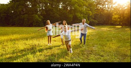 Glückliche Familie mit zwei Kindern, die laufen und Spaß im Sommerpark bei Sonnenuntergang haben. Stockfoto