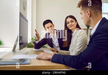 Team aus drei Geschäftsleuten, die mit Buchhaltungstabellen auf Bürocomputern arbeiten Stockfoto