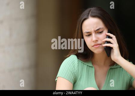 Verwirrte Frau, die draußen auf der Straße telefoniert Stockfoto
