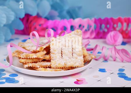 Gebratener italienischer Dessert-Snack für die Karnevalssaison namens 'Galani', 'Chiacchiere' oder 'Crostoli', je nach Region mit Papierschlangen im Hintergrund. Stockfoto