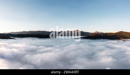 Nebelige Berglandschaft über den Wolken bei Sonnenuntergang. Luftaufnahme. Berggipfel ragen aus den Wolken hervor. Stockfoto