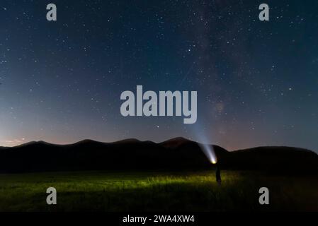 Sternenhimmel über Bergen und Mann mit Taschenlampe. Natürliche Landschaft. Stockfoto