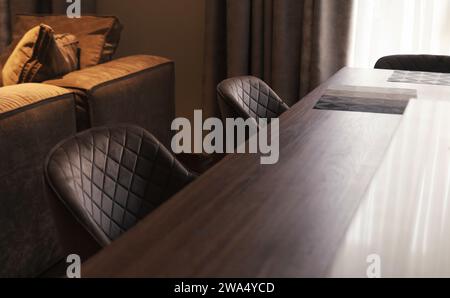 Großer Esstisch aus Holz mit weichen Stühlen. Innenraum der Küche. Stockfoto