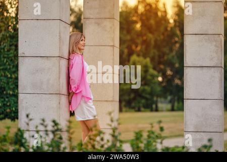 Eine nachdenkliche Frau, die sich an eine Steinsäule lehnt, ist während der goldenen Stunde in Gedanken verloren Stockfoto