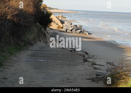 Blick auf den Rand der Access Road auf den Marrams, der aufgrund der Küstenerosion zusammenbrach, mit Menschen, die am Strand in Richtung Hex Block Seeschützung laufen. Stockfoto