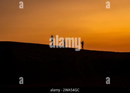 Touristen auf den Sanddünen, die in der Dämmerung hinter einander laufen. Stockfoto