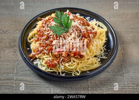 Spaghetti mit Soße Bolognese auf schwarzem Teller auf hölzernem Küchentisch Stockfoto