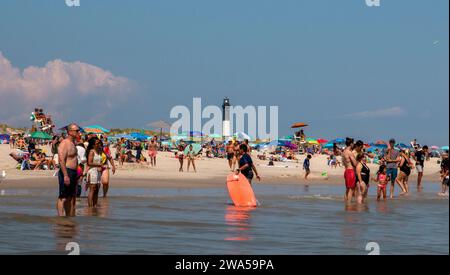 Bay Shore, New York, USA - 24. Juli 2021: Eine Gruppe von Menschen, die auf einem Sandstrand stehen, mit dem Fire Island Lighthouse im Hintergrund. Stockfoto