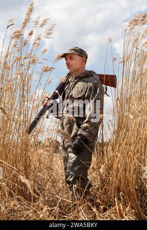 Im Spätherbst färbte sich das Gras am Ufer des Sees gelb. Der Entenjäger hält eine entladene Schrotflinte auf seiner Schulter. Er steht unter den Großen Stockfoto