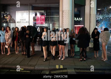 Junge Frauen stehen vor einem Nachtclub an einem nassen Silvesterabend im West End der Hauptstadt in London, England, Großbritannien. Stockfoto