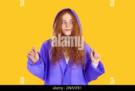 Lustiges rothaariges lockiges Teenager-Mädchen benutzt wasserdichte Regenjacke für Spaziergänge bei regnerischem Herbst. Stockfoto