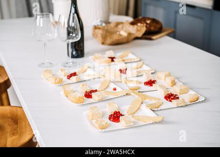 Vorspeisen mit Wein für ein Treffen zubereiten. Unfokussierte Hände arrangieren Käse und Brotvorspeisen auf einer Marmortheke mit einer leeren Weinflasche Stockfoto