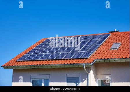 Solarzellen auf einem roten Dach vor blauem Himmel Stockfoto