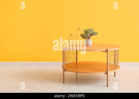 Hölzerner Kaffeetisch mit Bonsai-Baum und dekorativen Kerzenhaltern in der Nähe der orangefarbenen Wand Stockfoto